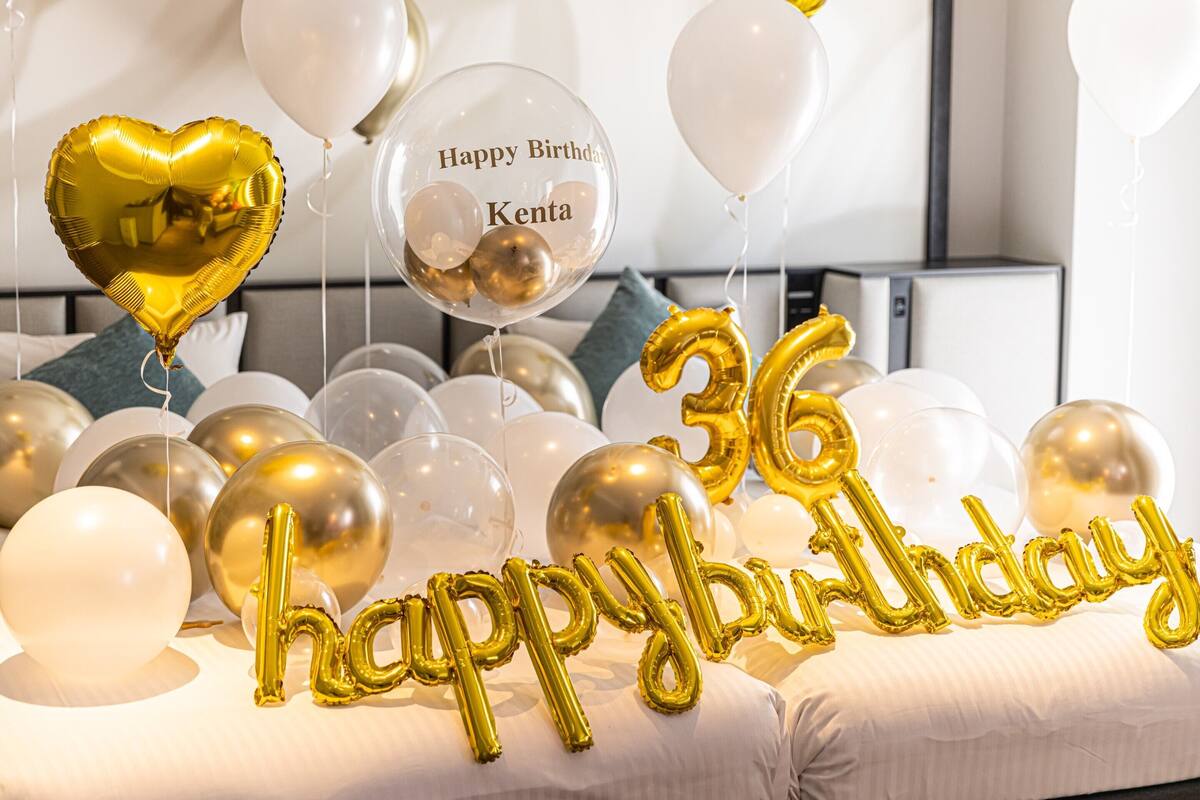 A room with a bed, balloons, and a 'Happy Birthday Kenta' balloon.