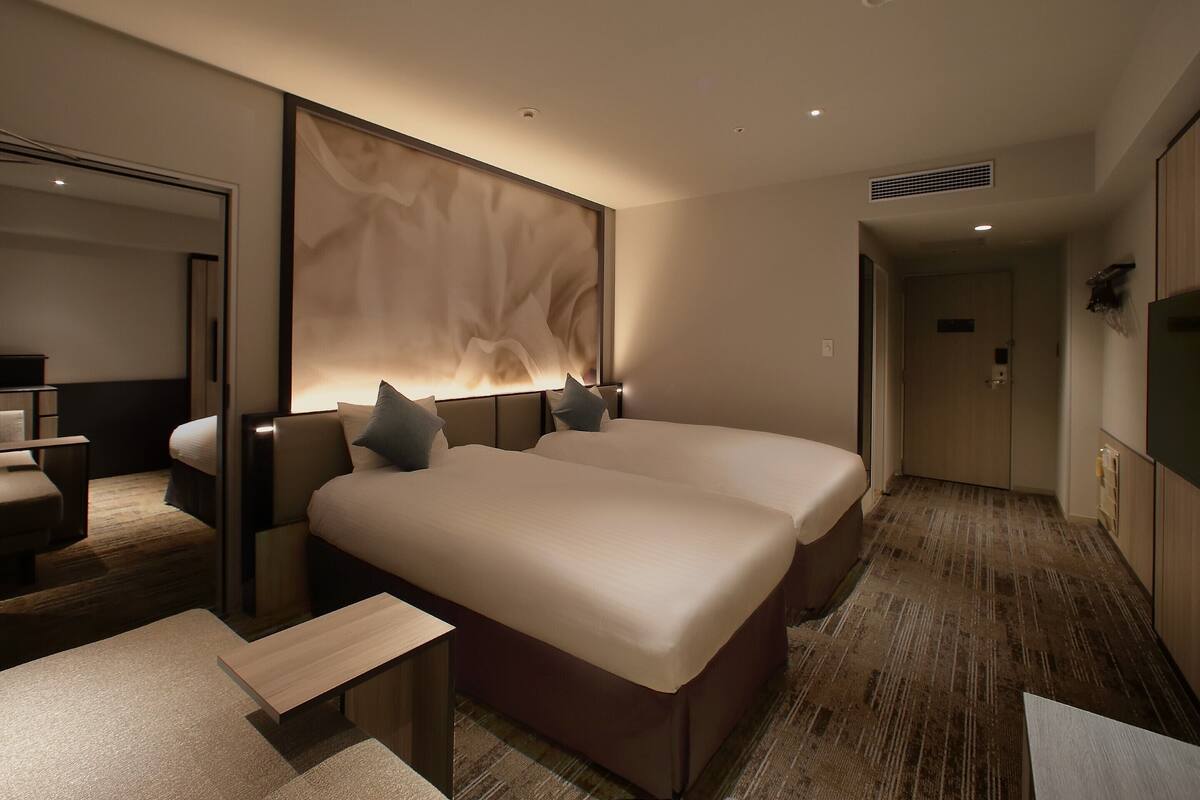 A modern hotel room with two beds, a desk, and a large mirror.