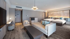 Une chambre d’hôtel moderne équipée d’un canapé, de deux lits, d’une télévision, d’un bureau et d’une grande fresque murale abstraite.