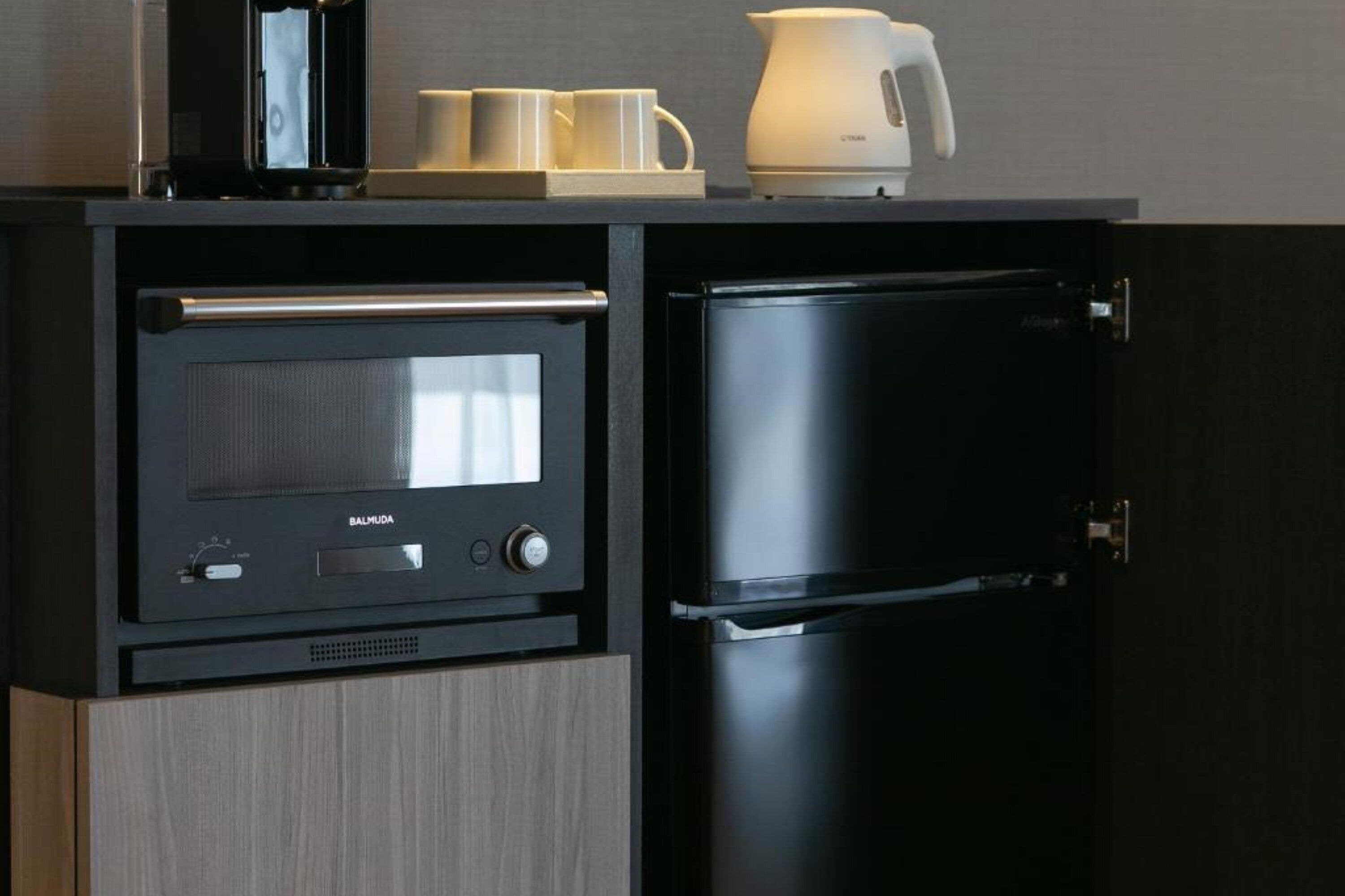 A compact kitchen with a built-in oven and refrigerator, a coffee maker, and two cups on the countertop.
