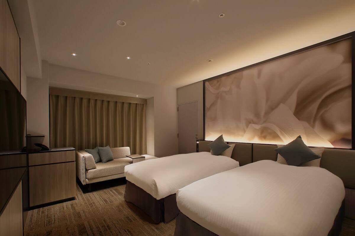 A hotel room with two beds, a sofa, a desk, and a large abstract wall art piece.