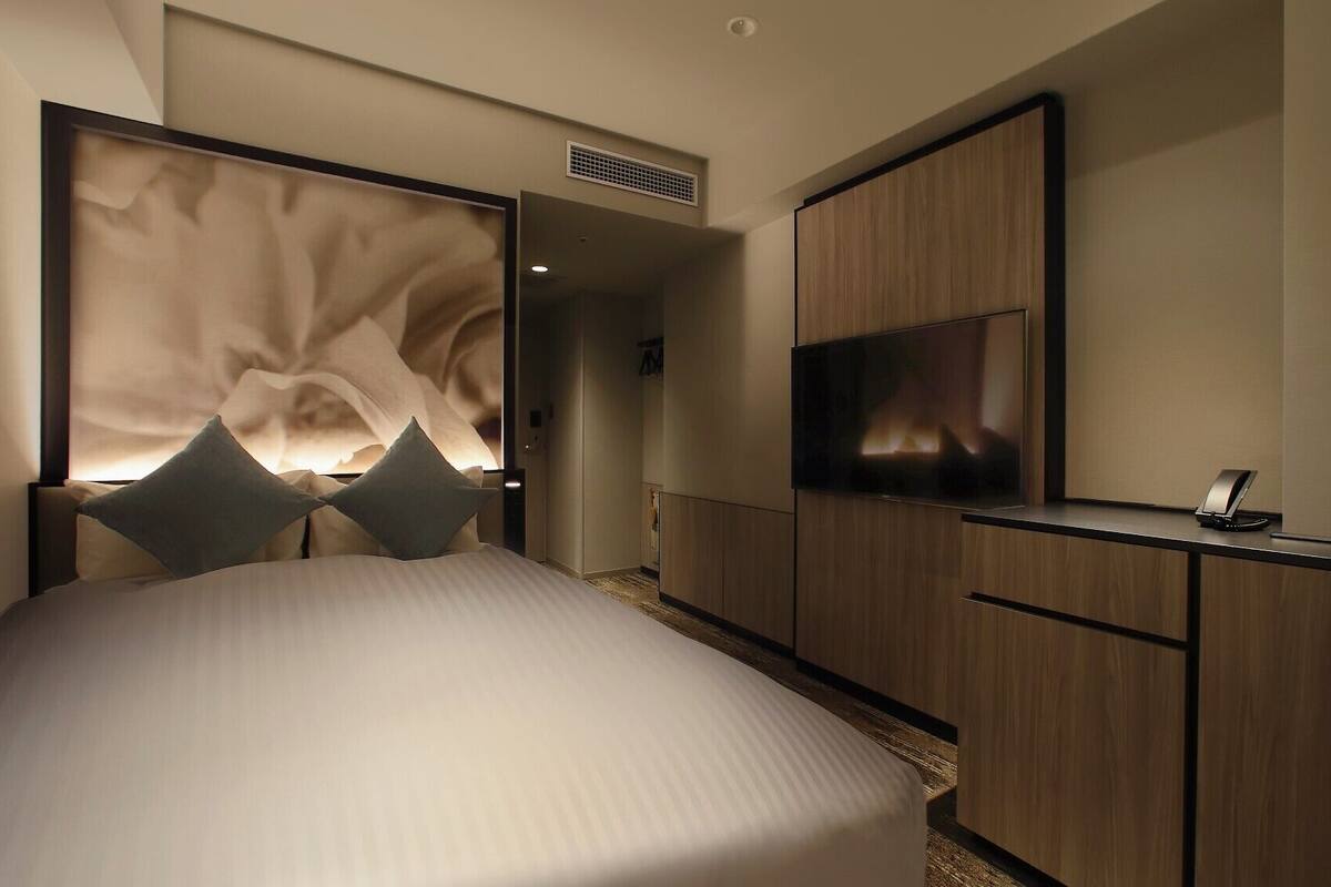 A modern hotel room with a large bed, a TV, and a desk with a telephone.