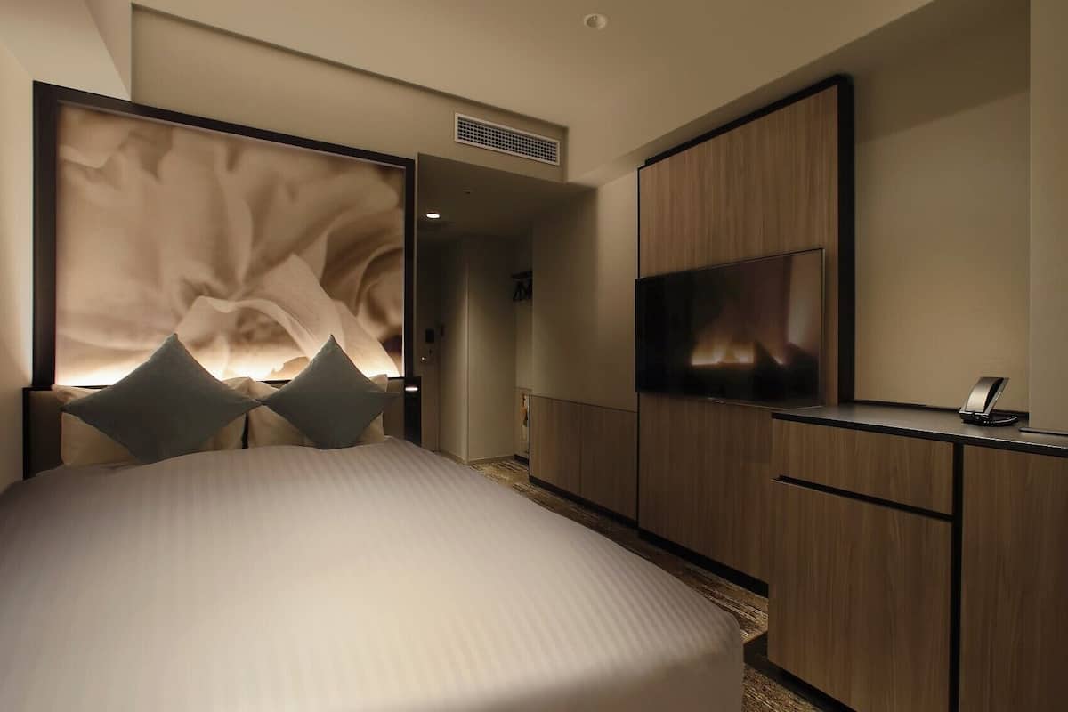 Ein modernes Hotelzimmer mit einem großen Bett, einem Fernseher und einem Schreibtisch mit Telefon.