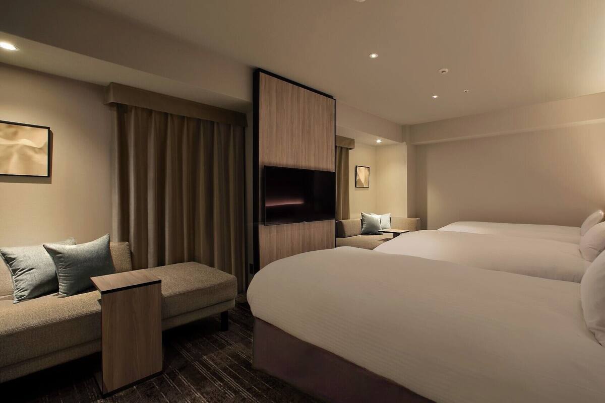 A hotel room with two beds, a sofa, a TV, and a desk.