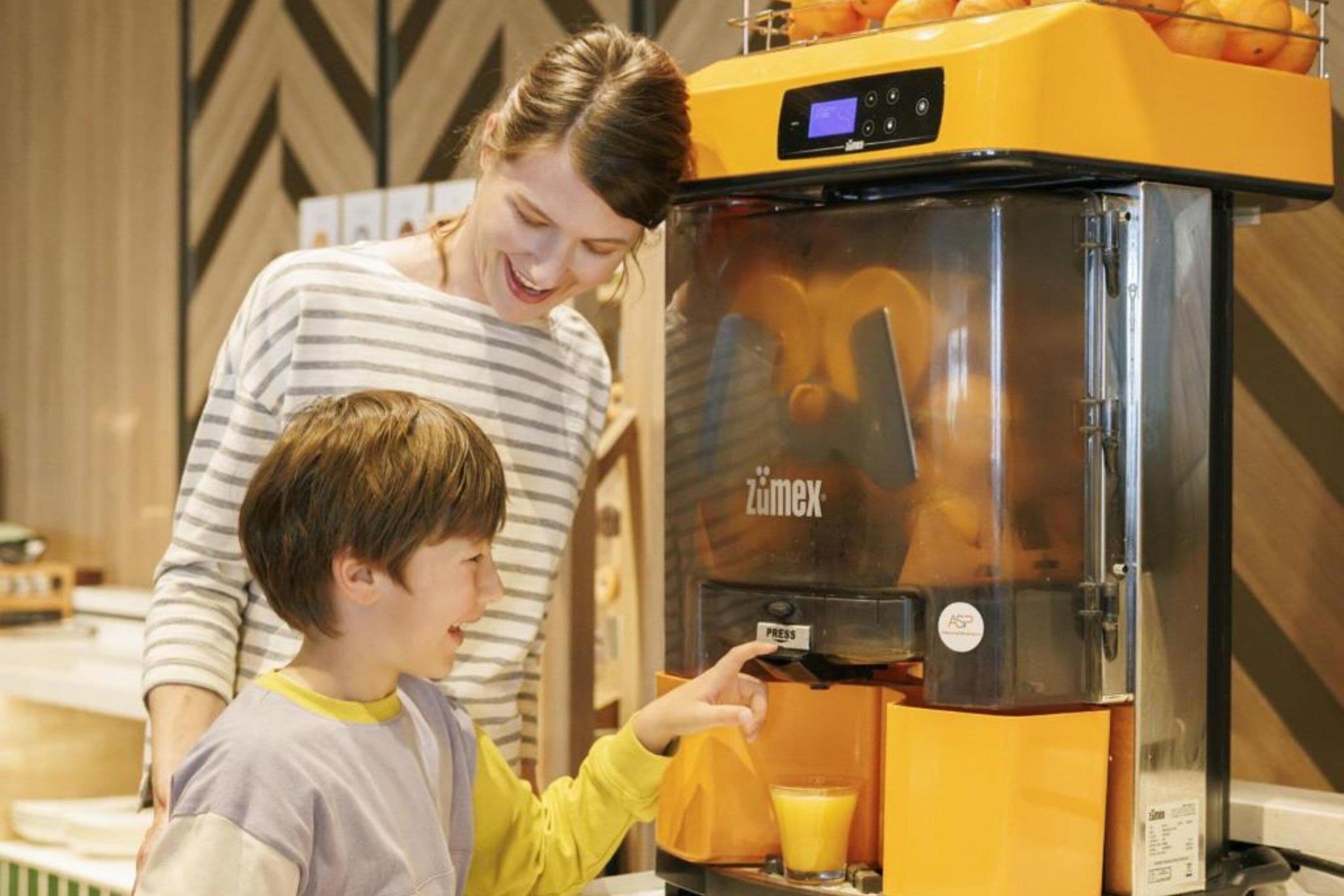 A person operating a juice press machine with a digital display and a glass of juice on the counter.