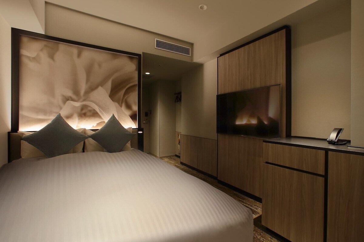 A modern hotel room with a bed, a TV, a desk, and a wardrobe.