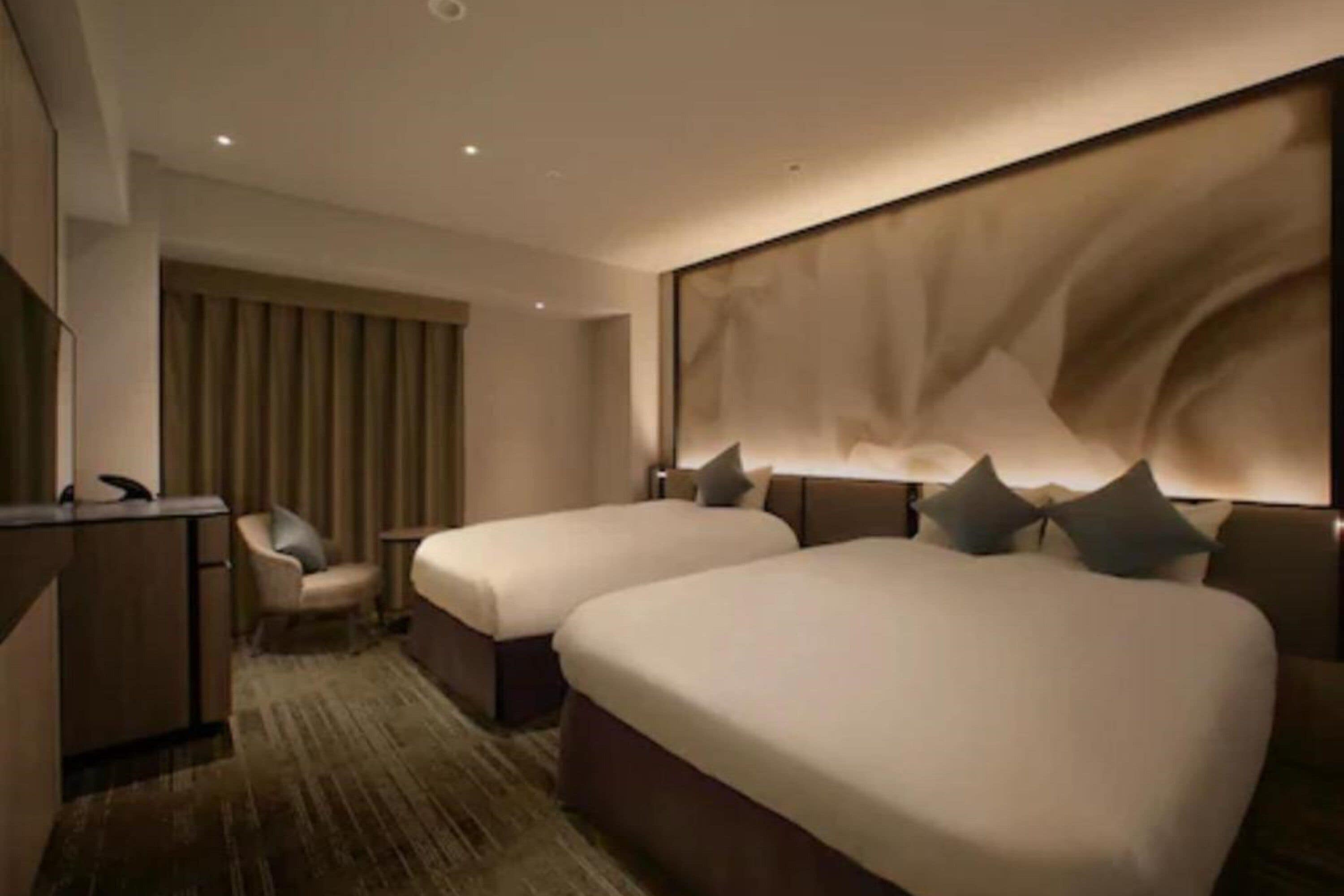 A hotel room with two beds, a desk, and a chair.