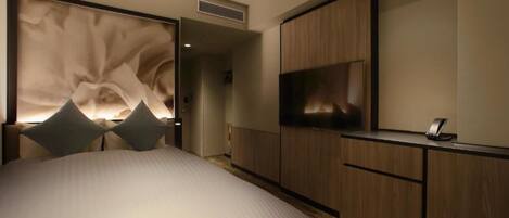 A modern hotel room with a large bed, a flat-screen TV, and a minibar.