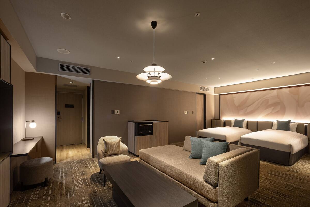 A modern hotel room with a sofa set, a TV, a coffee table, and a large bed.