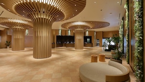 Un hall d’entrée spacieux agrémenté de structures modernes en bois au plafond, d’un espace salon central et de murs végétalisés.