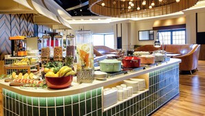 Un buffet proposant une variété de plats et de boissons, un espace détente avec des chaises au design moderne, et un luminaire décoratif au plafond.