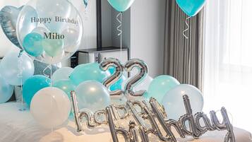 Un dormitorio con una cama, globos verde mar y blancos, y un globo con la inscripción 'Feliz Cumpleaños' y el nombre 'Mihos'.