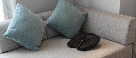 A grey sofa with two teal pillows and a black device on it.