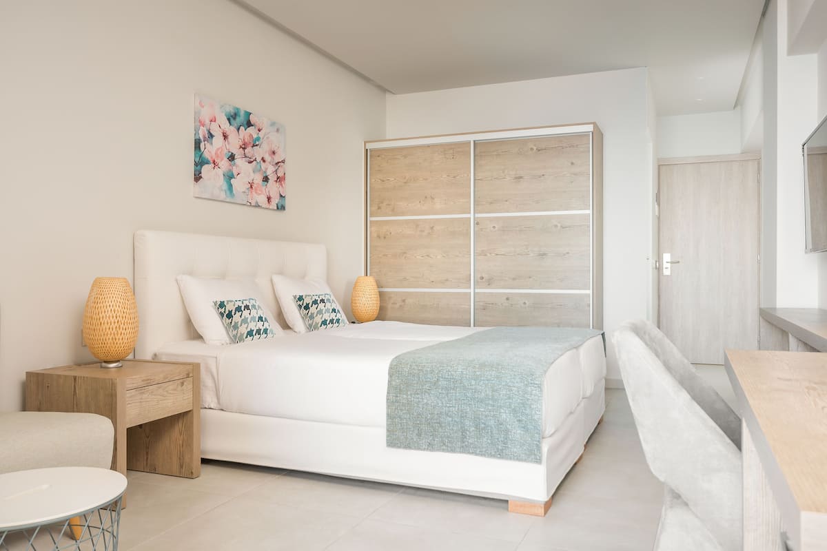 Quarto moderno com uma cama grande, um guarda-roupa de madeira, uma mesinha de cabeceira e um objeto decorativo na parede.