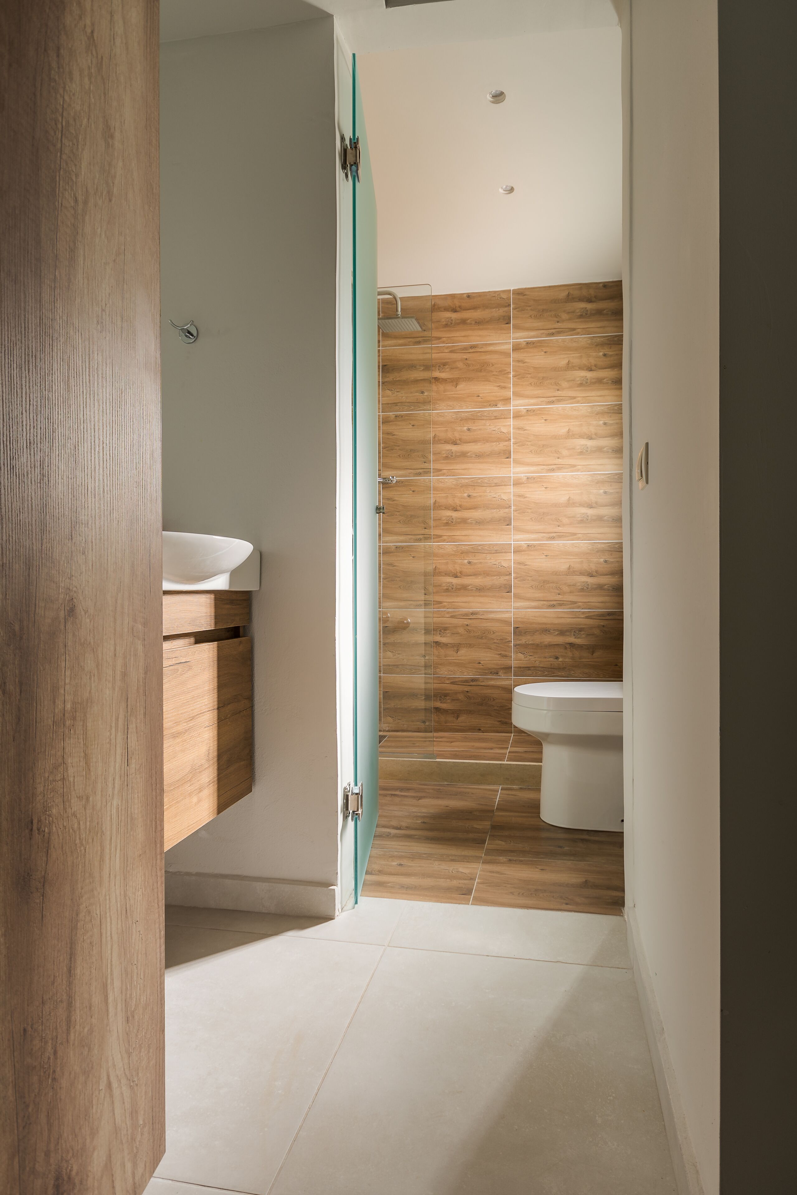 A modern bathroom with a wooden floor, a white sink, and a toilet.