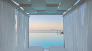 A view from a room with two white beds, a wooden floor, and white curtains, overlooking a calm body of water and a distant shoreline. - Golden Mare - All Inclusive (Corfu)