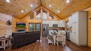A log cabin with a loft bedroom, a dining area, a kitchen with white cabinets, and a fireplace.
