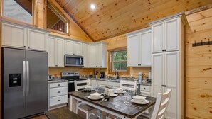 A kitchen with white cabinets, a stainless steel refrigerator, a microwave, and a dining table set with plates and glasses.