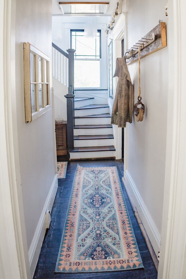 A hallway with a patterned rug, a staircase, and a coat hanging on the wall. - Beautiful, Restored Historic Craftsman House, Perfect for groups! (Birmingham)