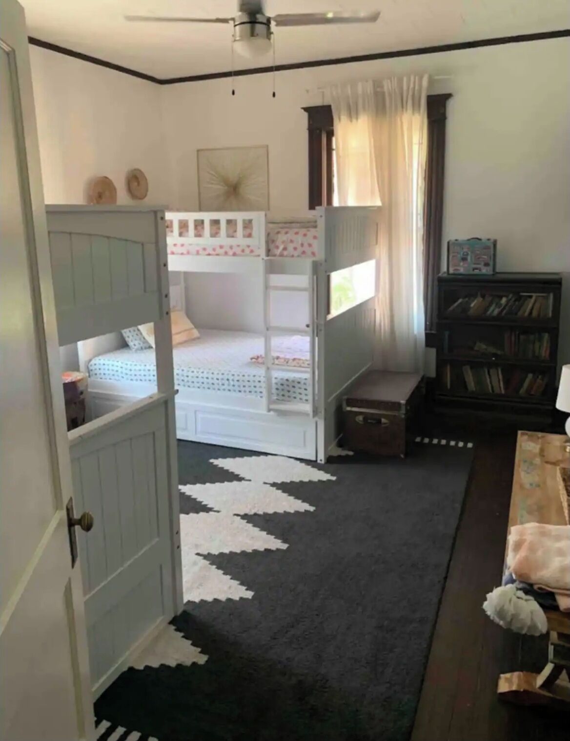 A bedroom with bunk beds, a bookshelf, and a patterned rug.
