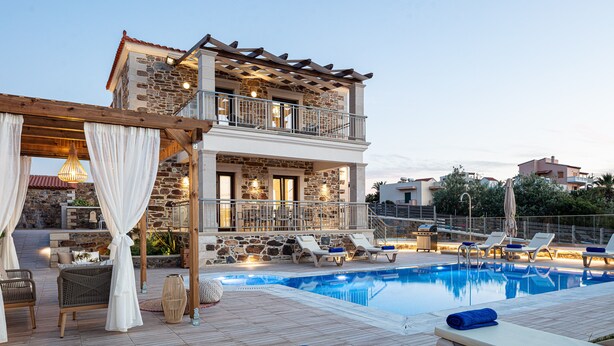 Um edifício de pedra com dois andares, piscina, área de estar externa e pérgola.