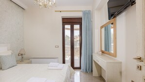 Quarto de hotel com cama, escrivaninha, espelho, lustre e porta para varanda.