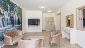 Uma sala de estar moderna com uma TV grande, duas poltronas confortáveis, uma mesa de centro de madeira e um mural com efeito de cachoeira na parede.