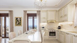 Uma sala de jantar ampla com uma mesa comprida e cadeiras, uma cozinha com bancadas de mármore e vista pelas portas de vidro.