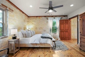 Ein Schlafzimmer mit Steinwand, einem hölzernen Bett, einem Deckenventilator und Blick ins Freie.