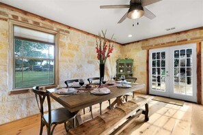 A dining area with a wooden table, chairs, a vase with flowers, and a view through a window. - Luxury w/Fire Pit-Amazing Views (Fredericksburg)