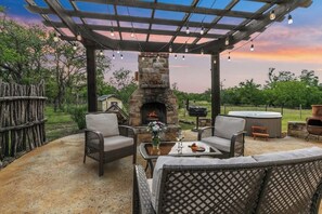 Un patio al aire libre con mobiliario de mimbre, una chimenea de piedra y un jacuzzi.