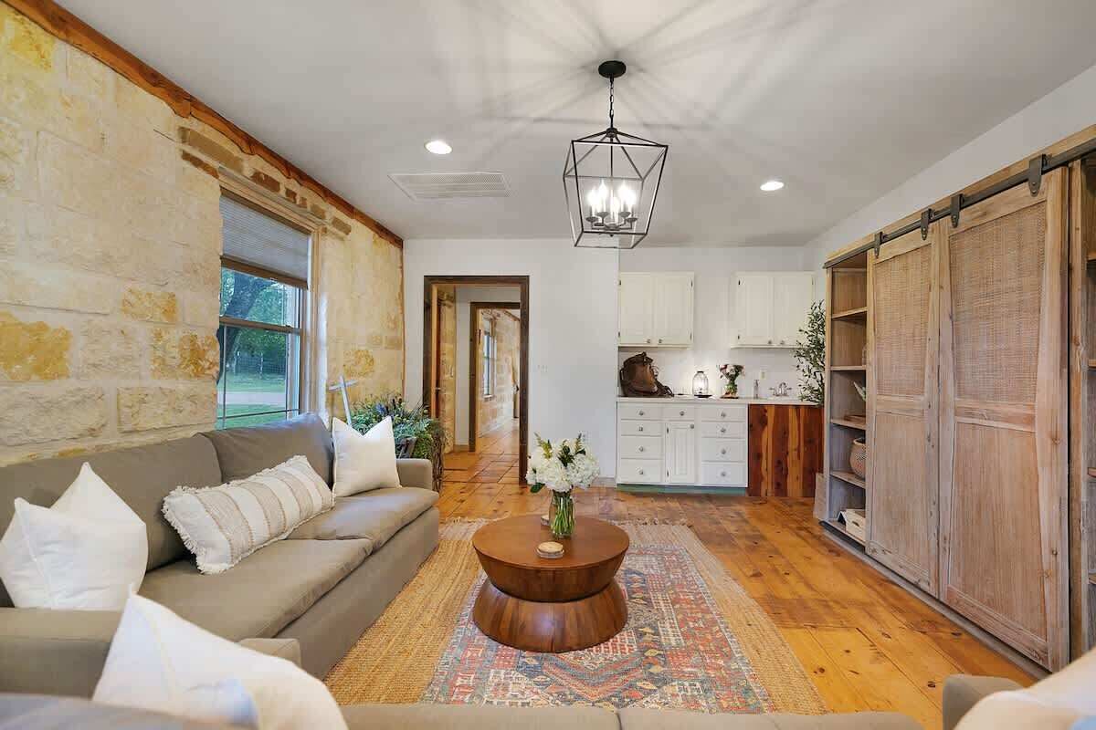 A spacious living room with a wooden floor, a beige sofa, a round coffee table, and a hanging light fixture.