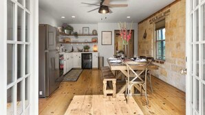 A kitchen with a wooden table, a ceiling fan, and stone walls.