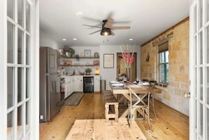 A kitchen with a wooden table, a ceiling fan, and stone walls.