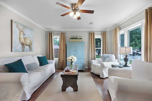 A living room with two white sofas, a wooden coffee table, a ceiling fan, and a light blue cabinet.
