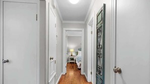 A narrow hallway with wooden flooring, white walls, and a door with a decorative metal handle. - Charming Home |4 Blks from Main (Fredericksburg)