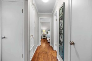 Un couloir étroit doté d’un plancher en bois, de murs blancs et d’une porte ornée d’une poignée en métal décorative.