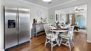 A modern kitchen with a stainless steel refrigerator, wooden dining table, and white chairs. - Charming Home |4 Blks from Main (Fredericksburg)