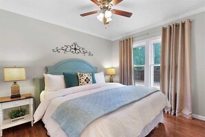 Un dormitorio con una cama, mesitas de noche, un ventilador de techo y una ventana con cortinas.