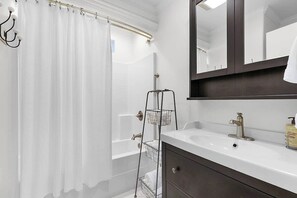 Un baño con una bañera blanca, un tocador oscuro, un espejo y un perchero para toallas.