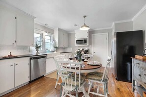 Una cocina con armarios blancos, un refrigerador negro y una mesa de comedor con sillas.