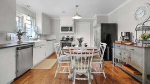 Una cocina moderna con armarios blancos, un comedor con una mesa redonda y sillas, un microondas, un refrigerador y un reloj en la pared.