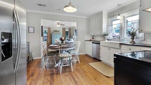 A modern kitchen with white cabinets, stainless steel appliances, and a dining area with a round table and white chairs. - Charming Home |4 Blks from Main (Fredericksburg)