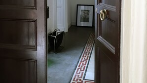 Un couloir avec un sol à motifs, un tableau encadré au mur et un luminaire suspendu au plafond.