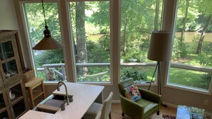 A spacious kitchen with a large island, a dining area with a green chair and a couch, and large windows offering a view of a garden and a pond. - Magical River Wonderland (Burnsville)