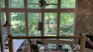 A room with large windows, a ceiling fan, a stone fireplace, and a dining area with a table and chairs. - Magical River Wonderland (Burnsville)