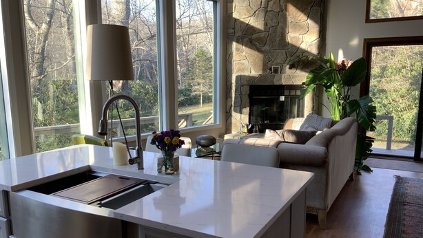 A modern kitchen with a large island, a stone fireplace, and a view of the outdoors. - Magical River Wonderland (Burnsville)