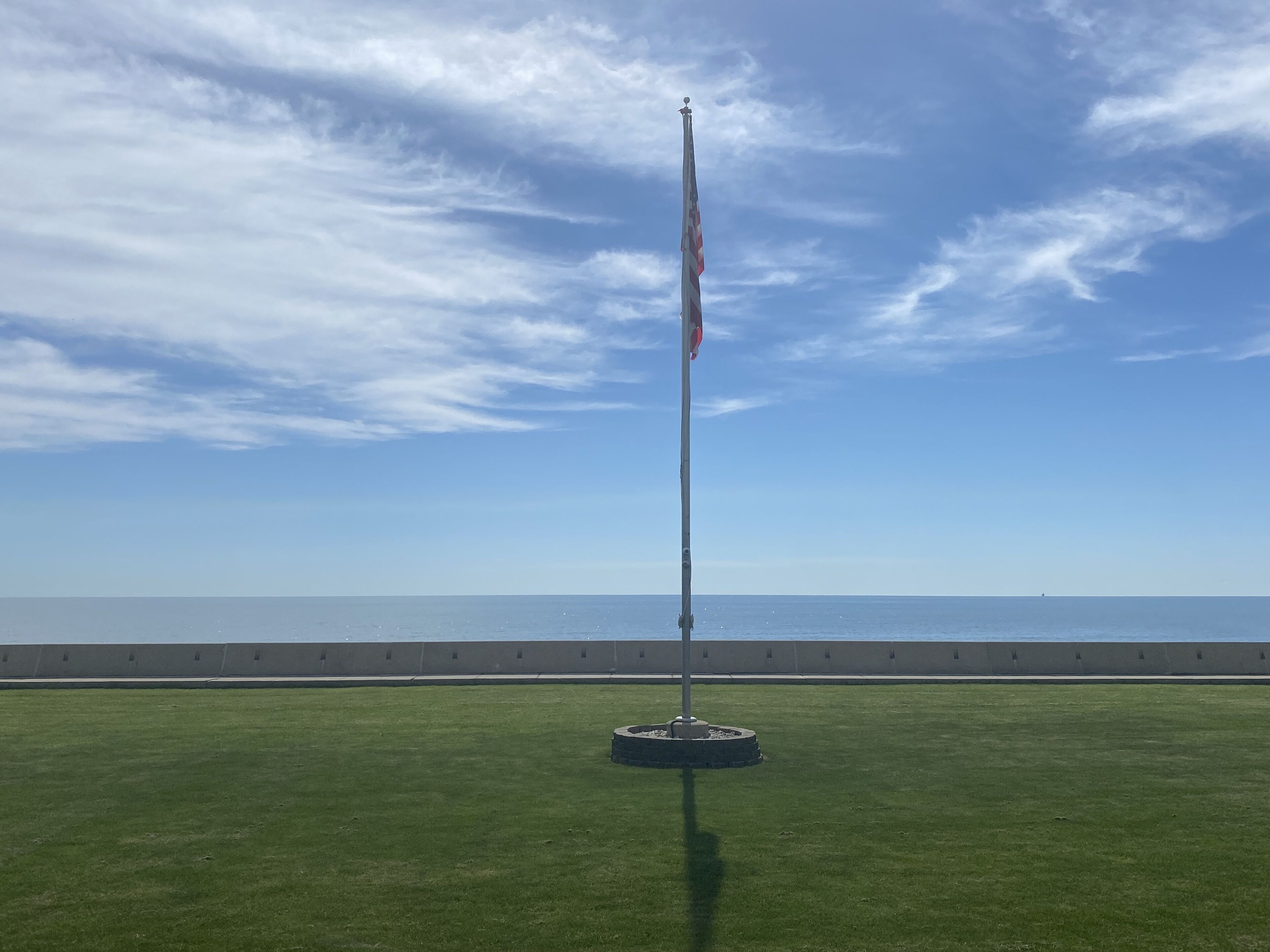 A flagpole on a grassy area with a clear sky and a distant view of the sea.
