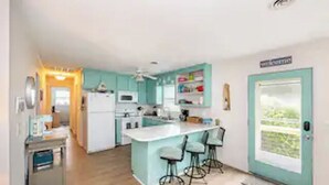 A modern kitchen with a central island, bar stools, and a view of the outdoors through a door. - DOG FRIENDLY - Second Row ...Ruff Life beach cottage. (Oak Island)