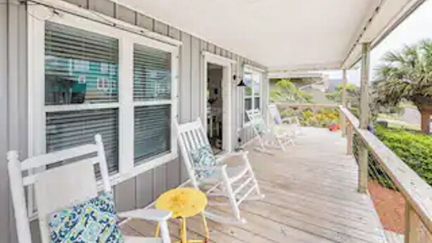 A covered porch with white rocking chairs and a yellow table. - DOG FRIENDLY - Second Row ...Ruff Life beach cottage. (Oak Island)